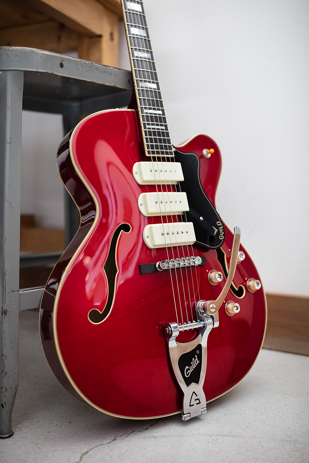 X-350 Stratford Scarlet Red electric guitar leaning against small metal stool and wood table