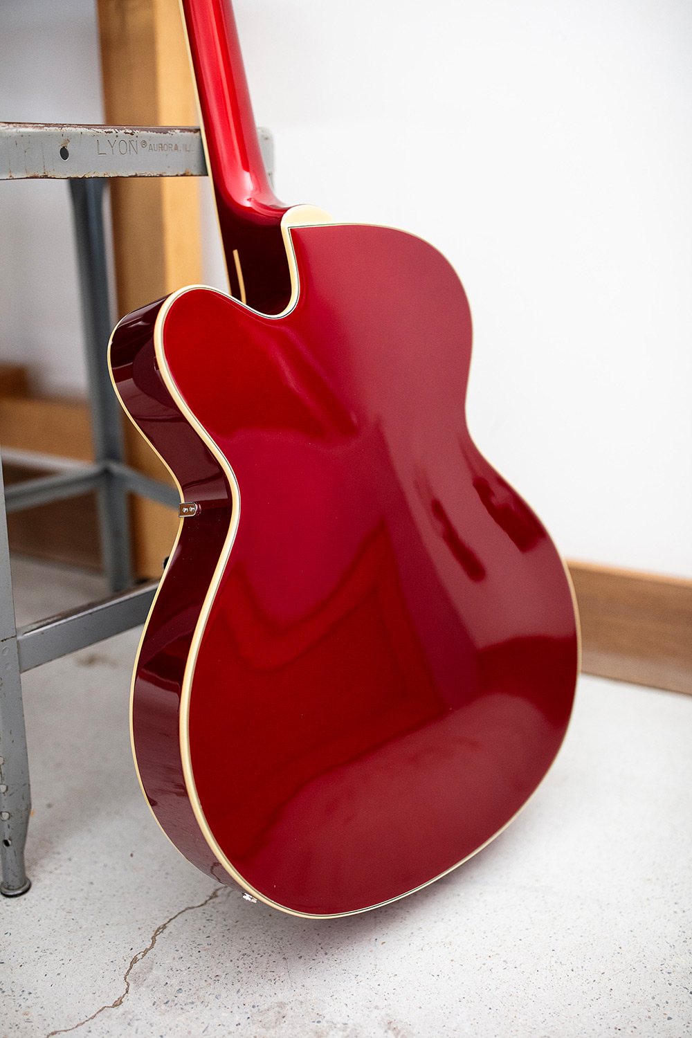 View of the back of the X-350 Stratford Scarlet Red electric guitar leaning against small metal stool and wood table