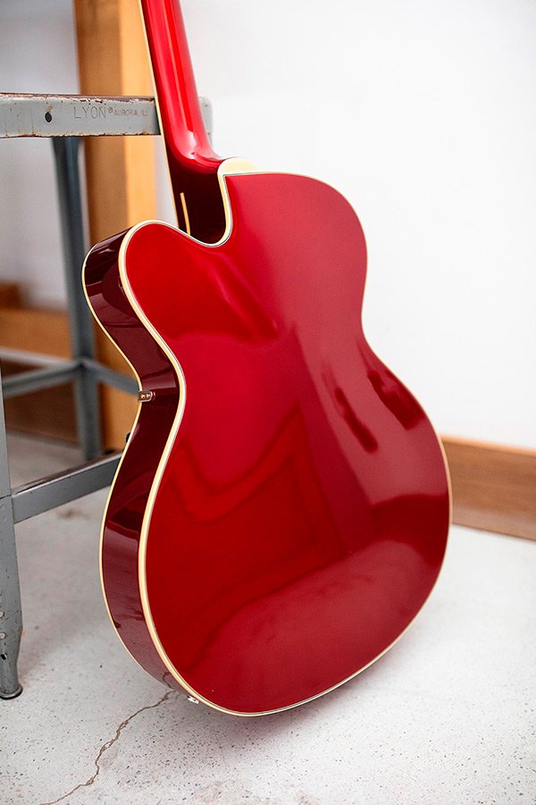 View of the back of the X-350 Stratford Scarlet Red electric guitar leaning against small metal stool and wood table thumbnail