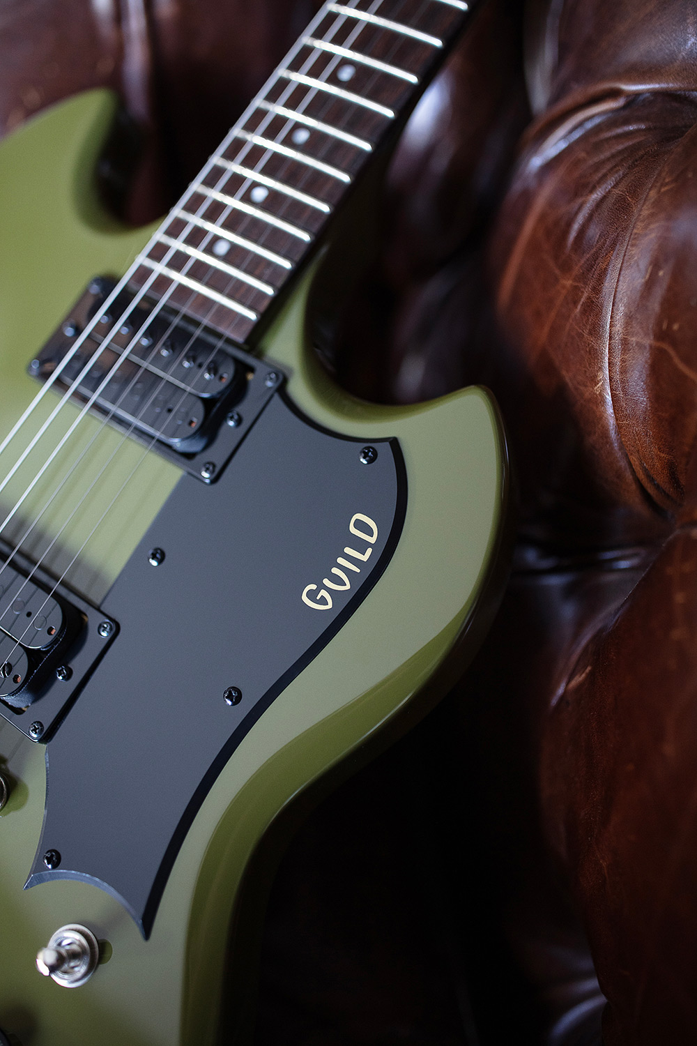 Close up of Polara Phantom Green pickguard with guitar laying on leather chair