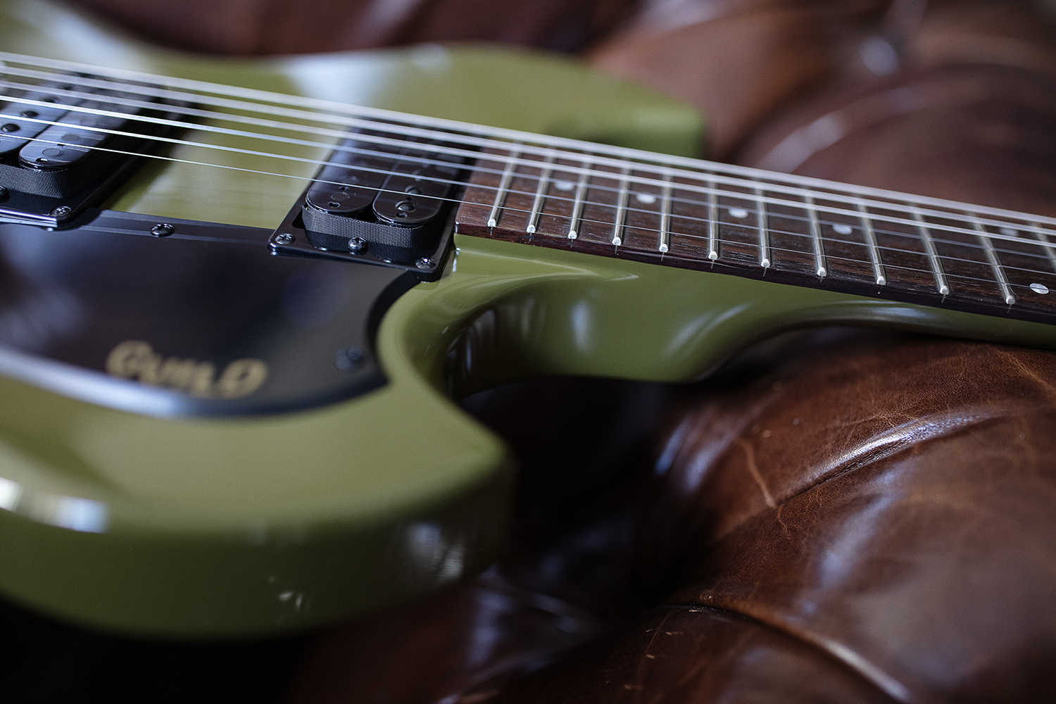 Close up of Polara Phantom Green nec, and strings with guitar laying on leather chair