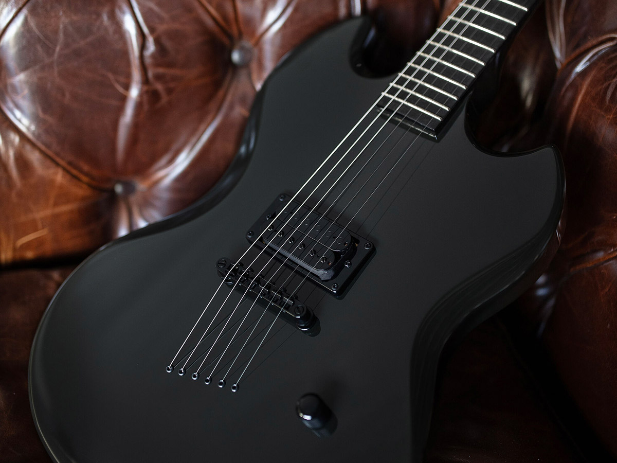 Polara Night Edition Tungsten guitar leaning on the arm of a leather couch