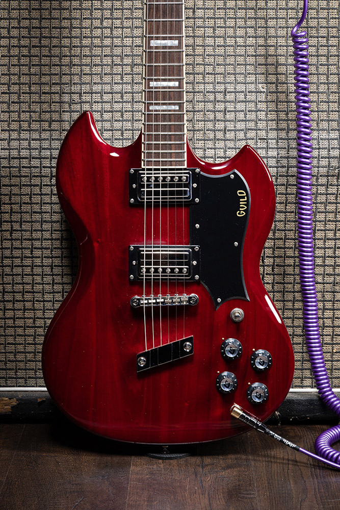View of Polara Deluxe Cherry Red leaning on an amp with a purple coiled plug