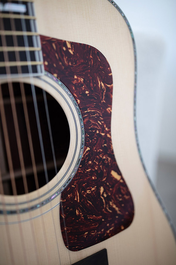 Close-up of GSR D-55 70th Anniversary Limited acoustic guitar's body, featuring a decorative pickguard with a marbled design and visible strings.