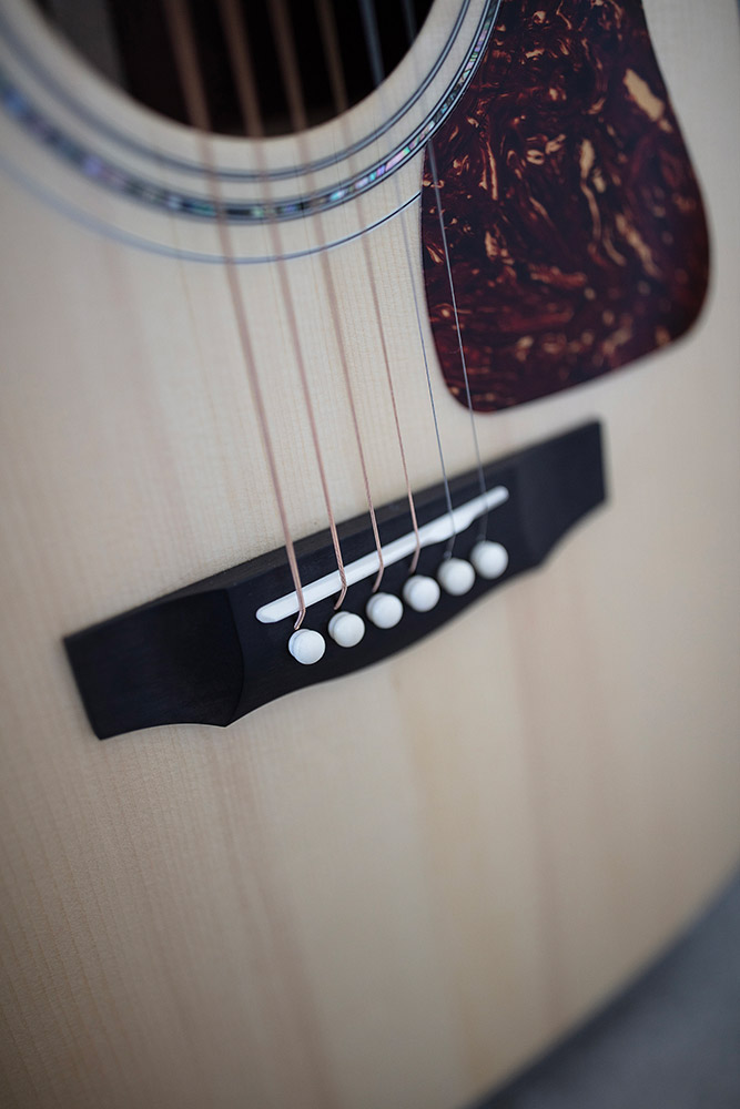 Close-up of GSR D-55 70th Anniversary Limited acoustic guitar's bridge and strings, showcasing the wood grain and decorative pickguard.