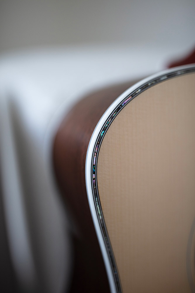 Close-up of GSR D-55 70th Anniversary Limited acoustic guitar's body, showcasing intricate inlay details along the edge. Soft background blur.