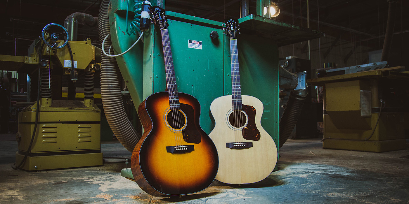 F-40 Natural and Antique Burst acoustic guitars positioned in guitar workshop with machinery in the background.