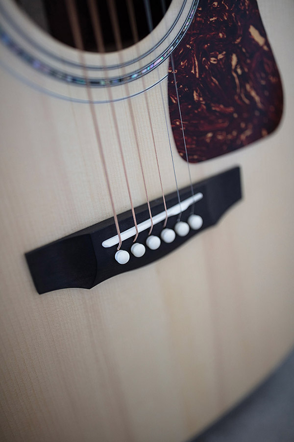 Close-up of GSR D-55 70th Anniversary Limited acoustic guitar's bridge and strings, showcasing the wood grain and decorative pickguard.