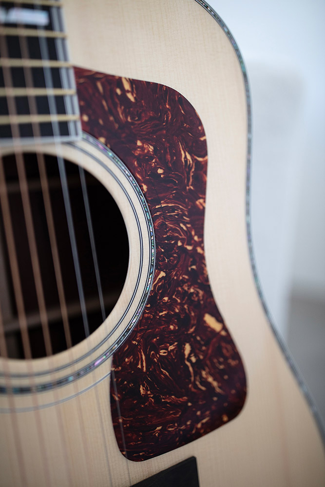 Close-up of GSR D-55 70th Anniversary Limited acoustic guitar's body, featuring a decorative pickguard with a marbled design and visible strings.