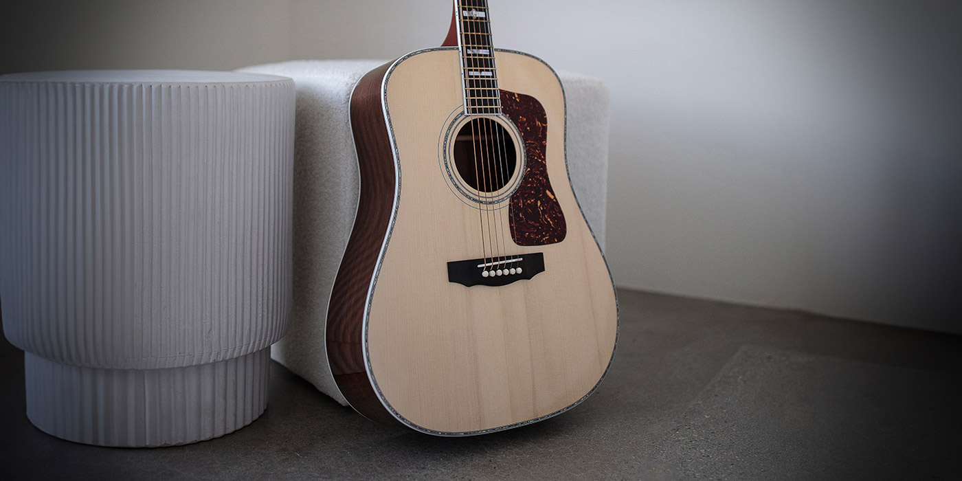 A close-up of GSR D-55 70th Anniversary Limited acoustic guitar leaning against a textured white stool in a minimalist setting.