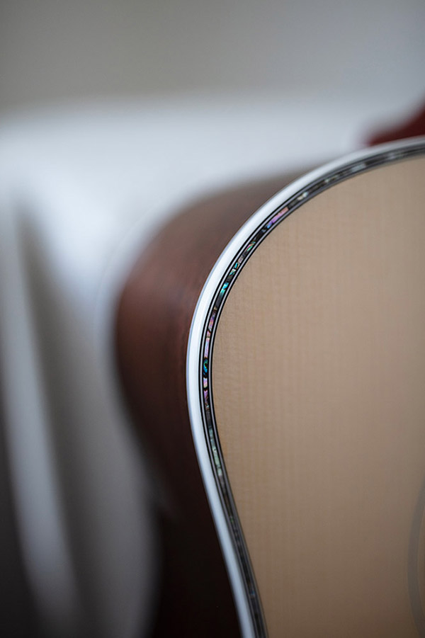 Close-up of GSR D-55 70th Anniversary Limited acoustic guitar's body, showcasing intricate inlay details along the edge. Soft background blur.