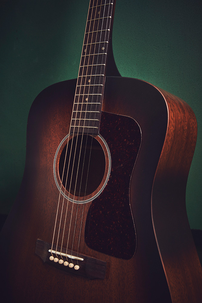Close-up of D-20 acoustic guitar with antique burst wood finish. The background is a gradient green.