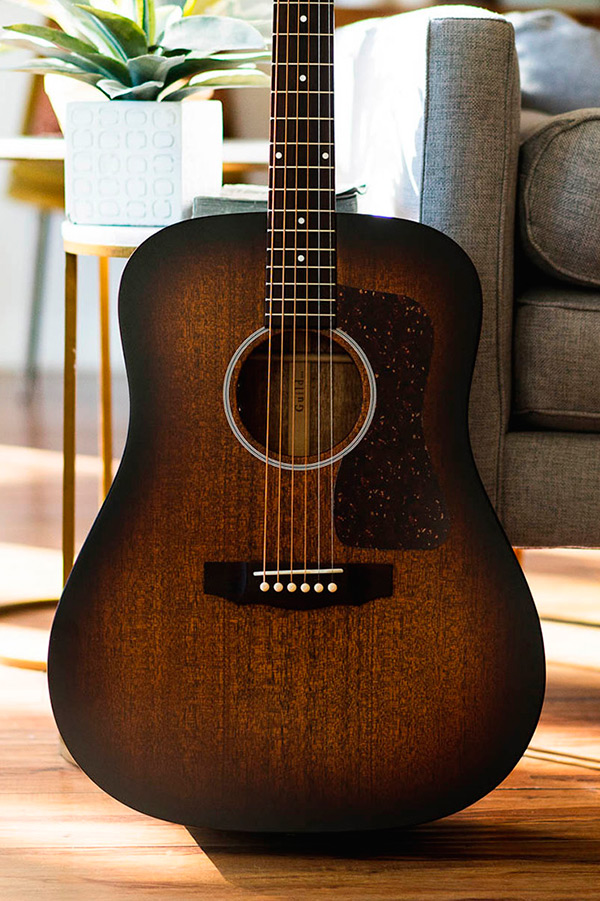 Body of D-20 acoustic guitar with antique burst wood finish, placed near a potted plant and a cozy sofa.